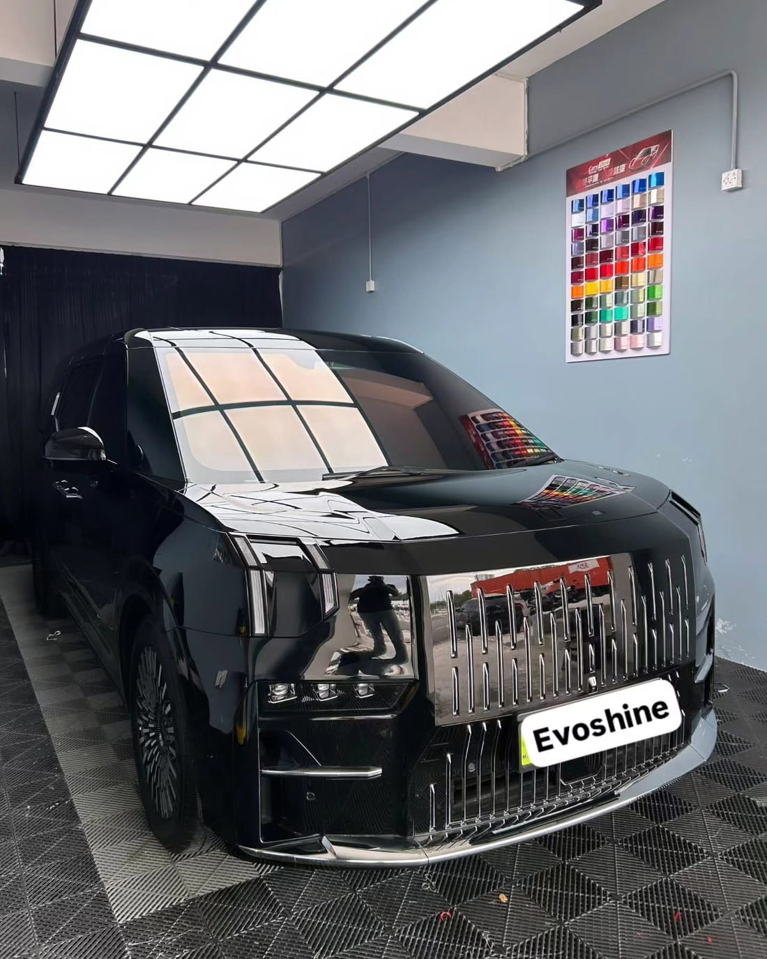 A black Zeekr 009 MPV finished under the ceiling light panel of the Evo Shine Kajang bay, with the workshop colour-wrap swatch chart on the wall behind it.